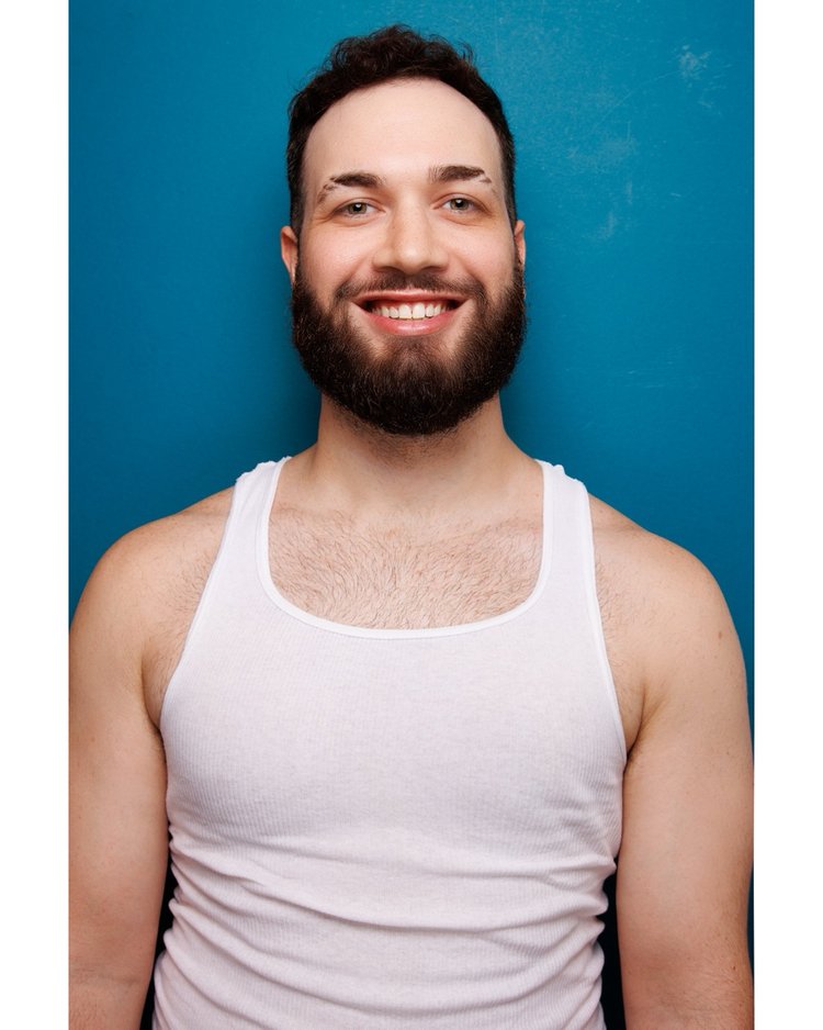 Thomas James smiling in a white tank against a blue backdrop